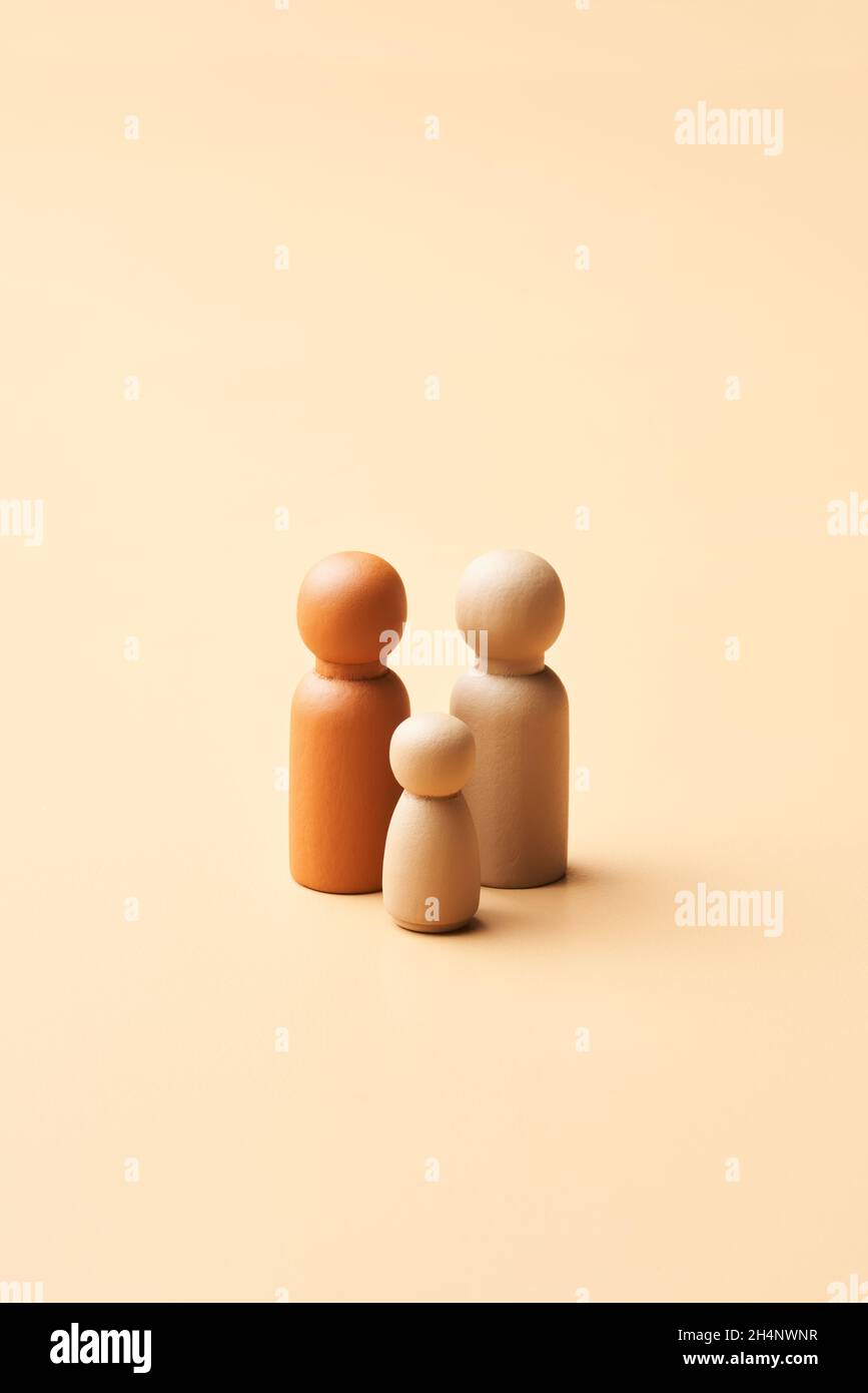 Semplici figurine in legno di coppia gay multirazziale con capretto che rappresentano la famiglia omoparentale su sfondo beige Foto Stock
