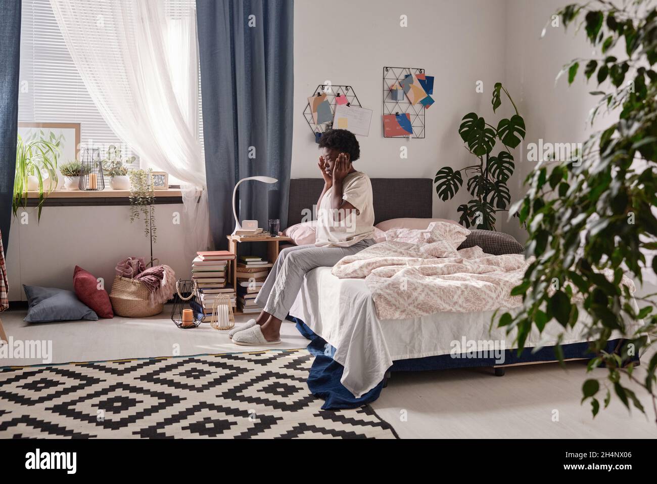 Giovane donna africana seduta sul letto con mal di testa, che ha un aspetto stanco e andare a letto Foto Stock