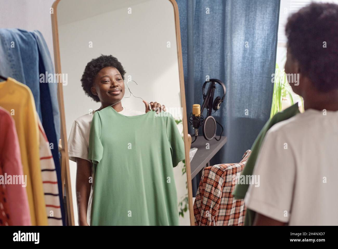 Giovane donna africana in piedi davanti allo specchio e provare sul nuovo vestito mentre si alza in piedi nella stanza Foto Stock