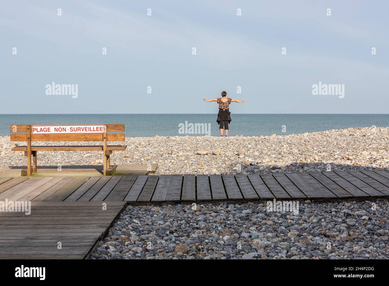 Lady sola di fronte al mare, facendo movimenti di braccio, su una spiaggia di ciottoli a Cayeux-sur-Mer. Opal Coast, Francia Foto Stock