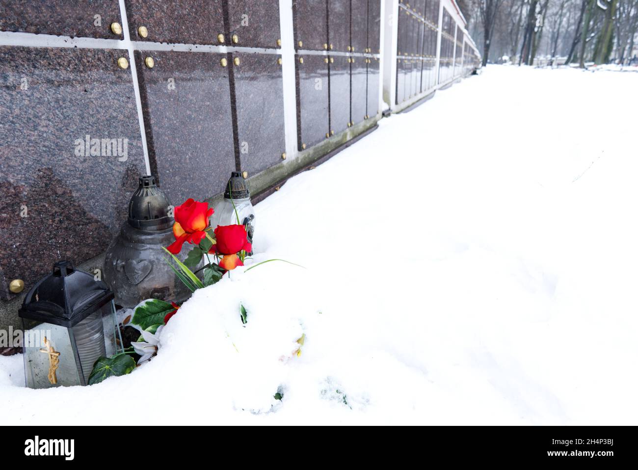 fiori e candele di fronte al muro di colombario in cimitero nella neve in inverno Foto Stock