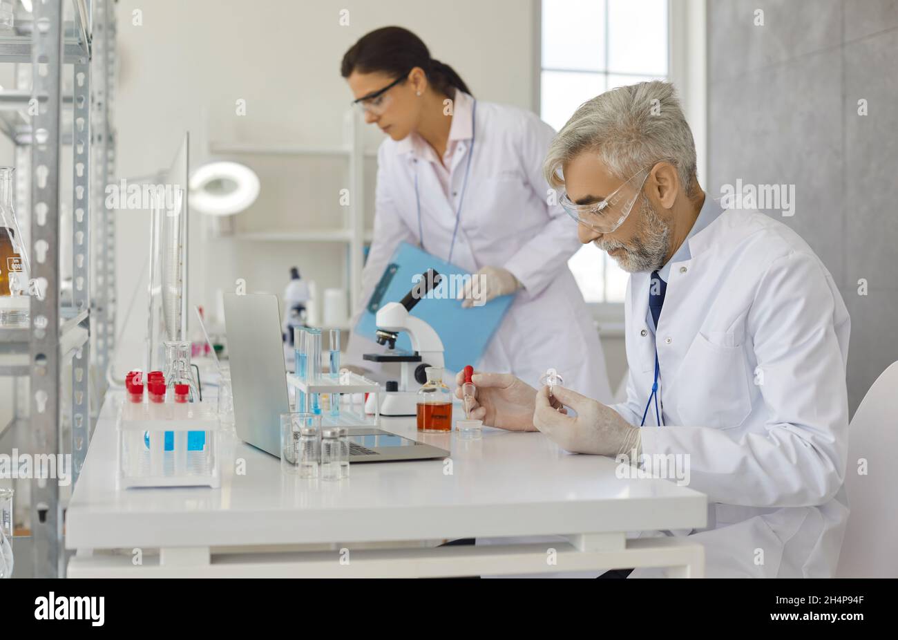 Scienziato maschile senior che fa esperimenti in laboratorio pipettando campioni di terreno di coltura cellulare. Foto Stock