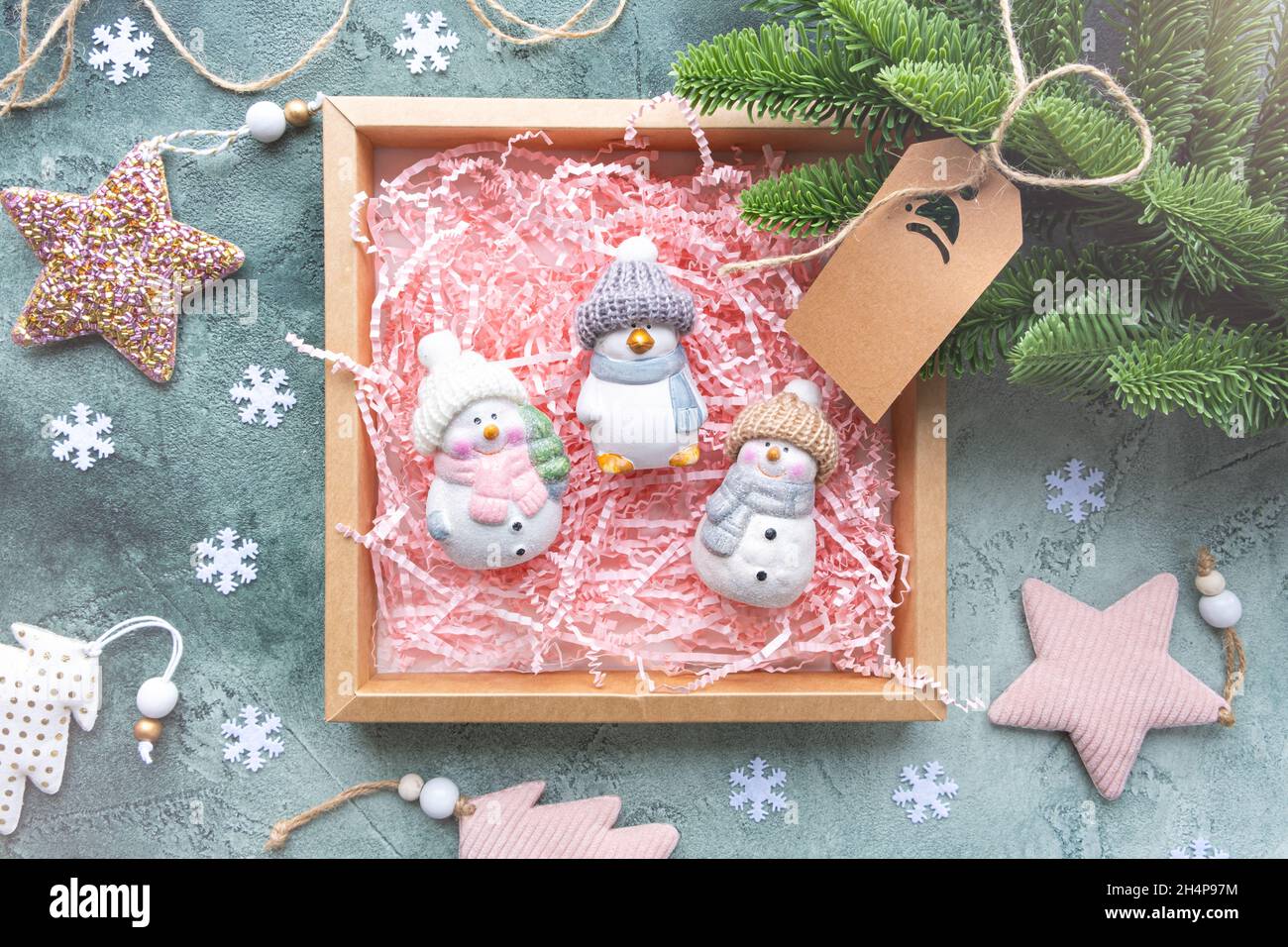 Confezione regalo con giocattoli su sfondo verde con decorazioni natalizie. Ci sono tre giocattoli in ceramica in una scatola con un riempitivo di carta rosa, pupazzi di neve e un pinguino Foto Stock