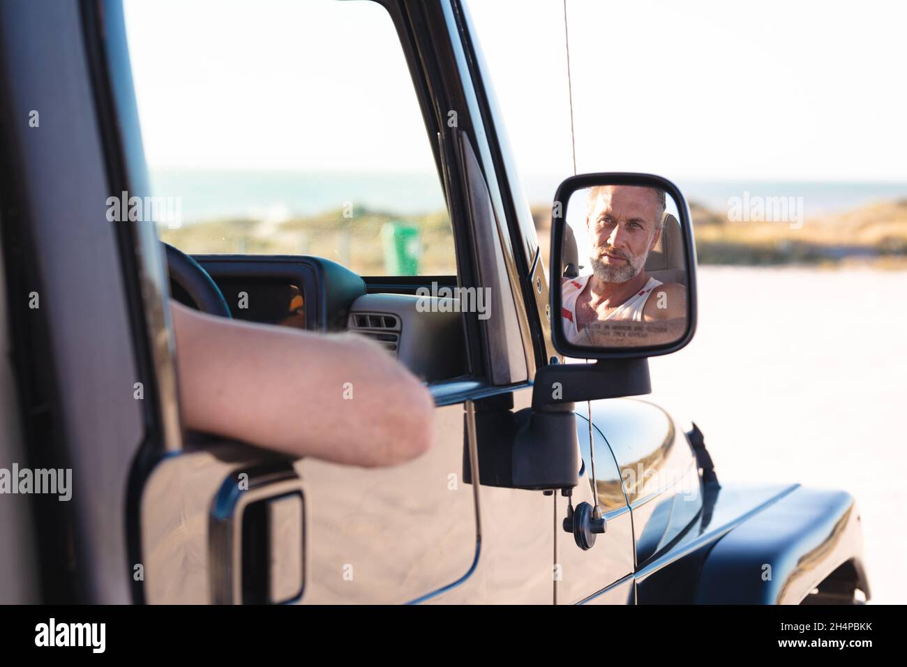 Ritratto di uomo caucasico sorridente in auto riflesso in specchio laterale in giornata di sole al mare Foto Stock