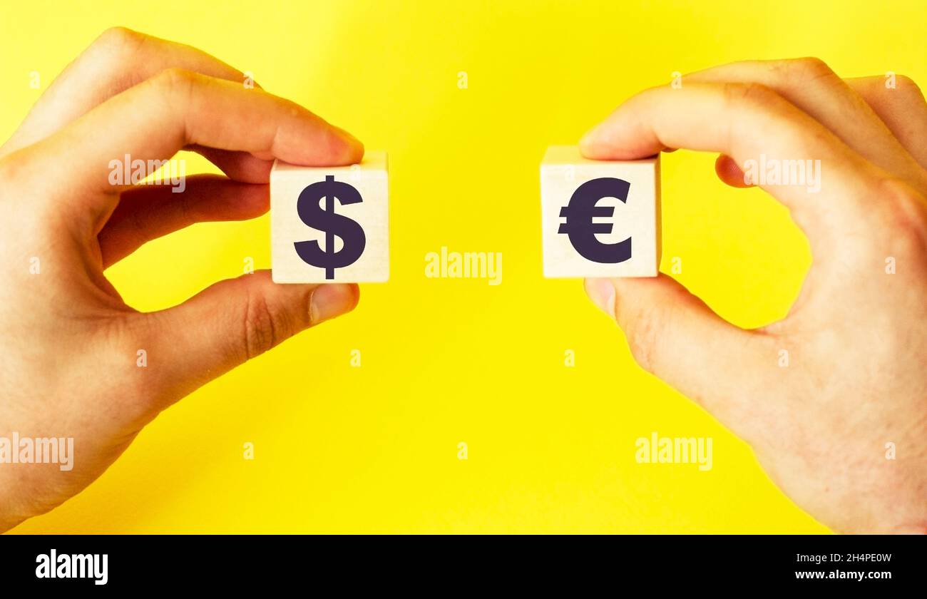 Mano con cubetti di legno e testo euro e dollaro su sfondo giallo Foto Stock