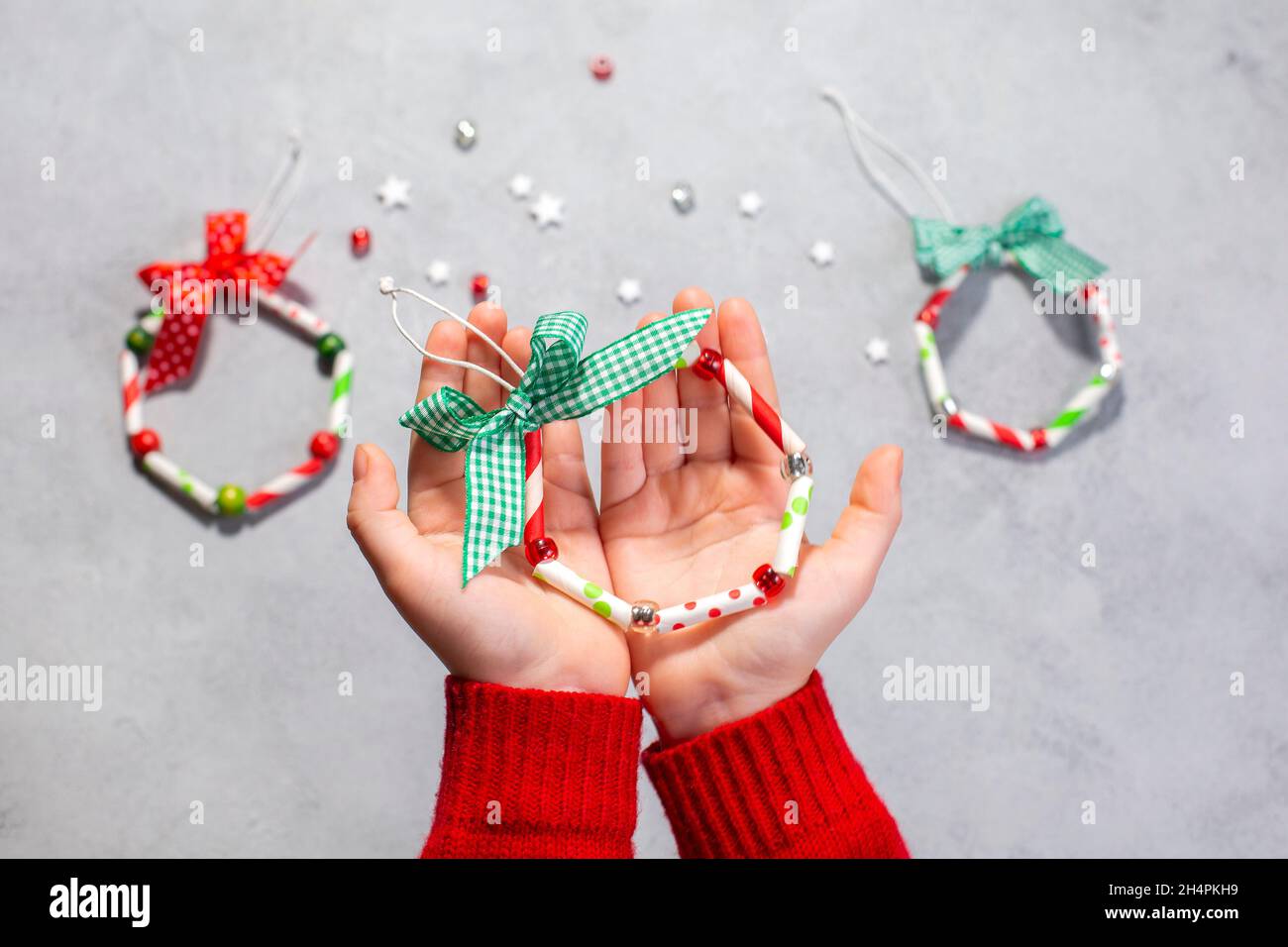 Ormamenti della corona di Natale dalla paglia di carta. Istruzioni dettagliate. Fase 7 le mani dei bambini mostrano il prodotto finito. Hobby a casa. Foto Stock