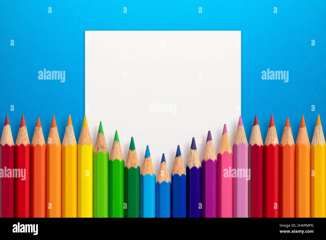 Layout creativo composto da matite a colori su sfondo di carta blu con cartoncino bianco. Disposizione piatta. Concetto di istruzione. Foto Stock
