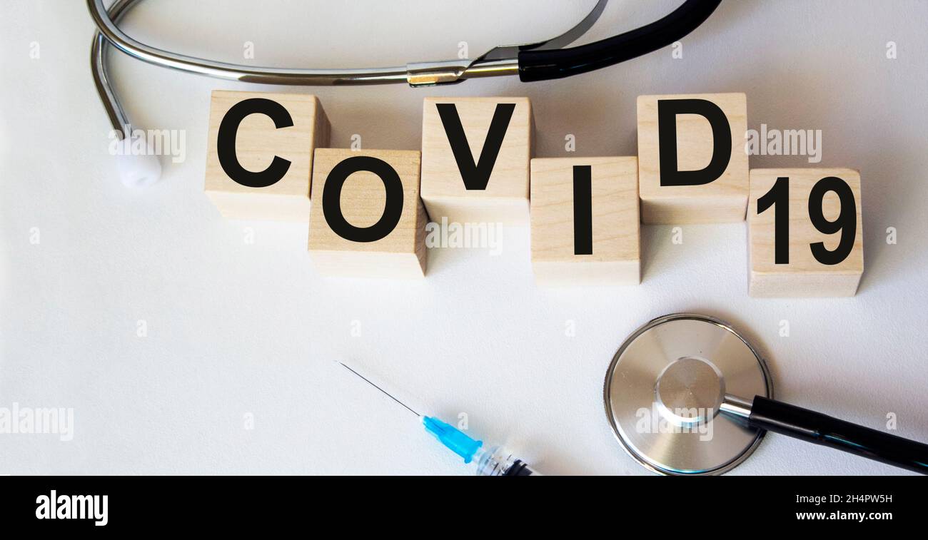 Testo su blocchi di legno COVID-19, sfondo bianco e con siringa medica, stetoscopio Pandemic concetto. Foto Stock