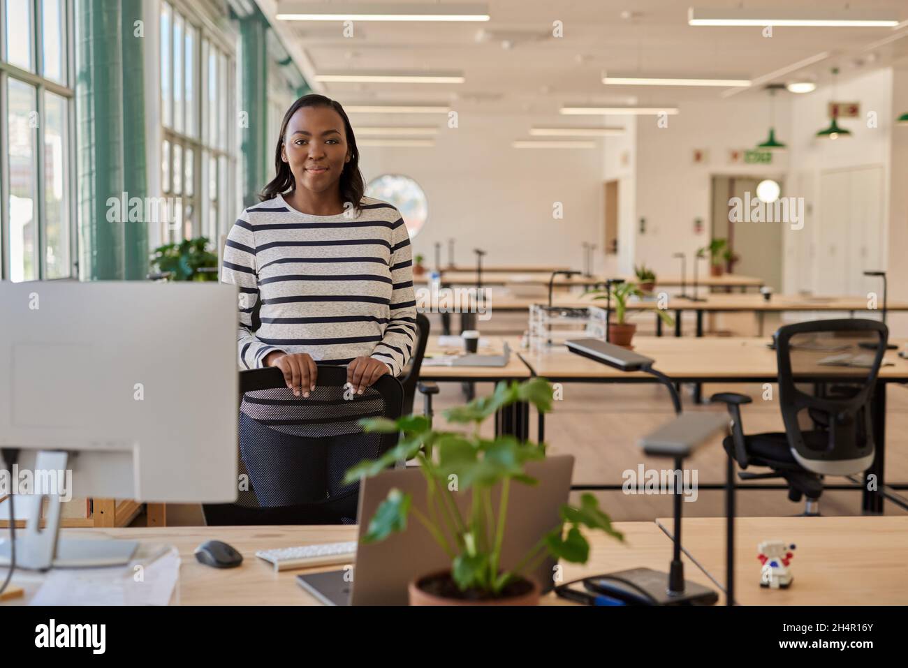 Fidata giovane donna d'affari africana in piedi alla sua scrivania in un ufficio Foto Stock