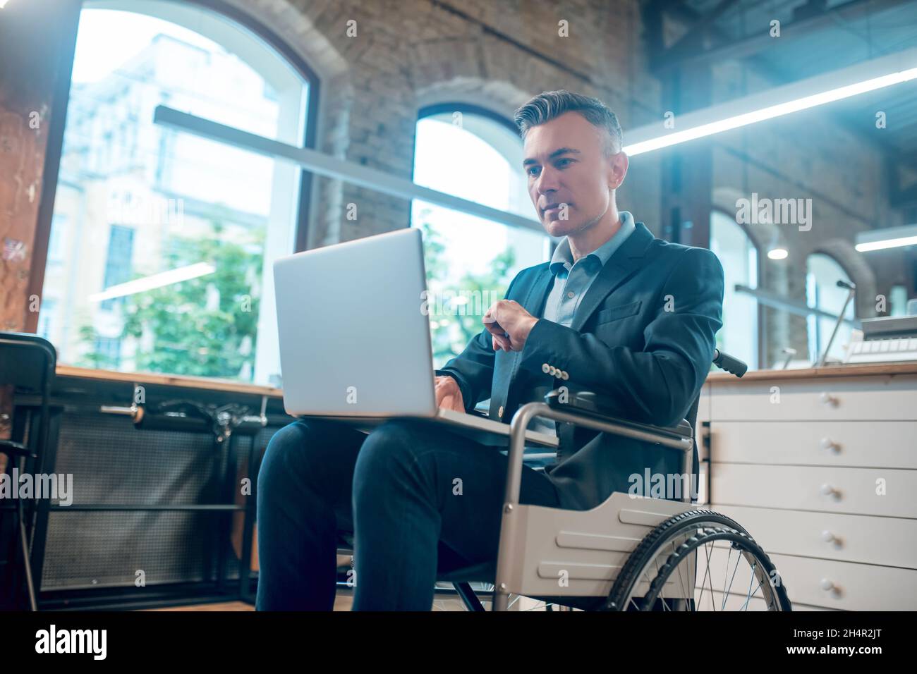 Uomo disabile in sedia a rotelle che lavora su un computer portatile Foto Stock