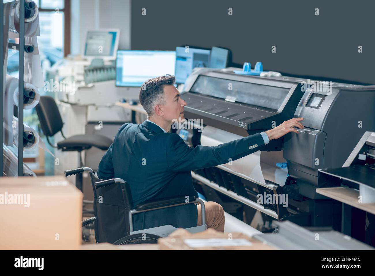 Profilo dell'uomo in sedia a rotelle che tocca i pannelli di controllo della stampante Foto Stock