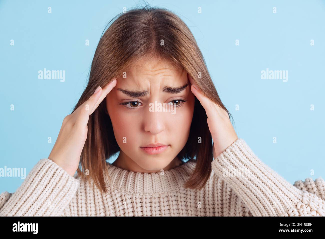 Ritratto di mezza lunghezza di giovane ragazza beuatiful, studente in felpa con cappuccio marrone ha un mal di testa isolato su sfondo studio blu chiaro. Foto Stock