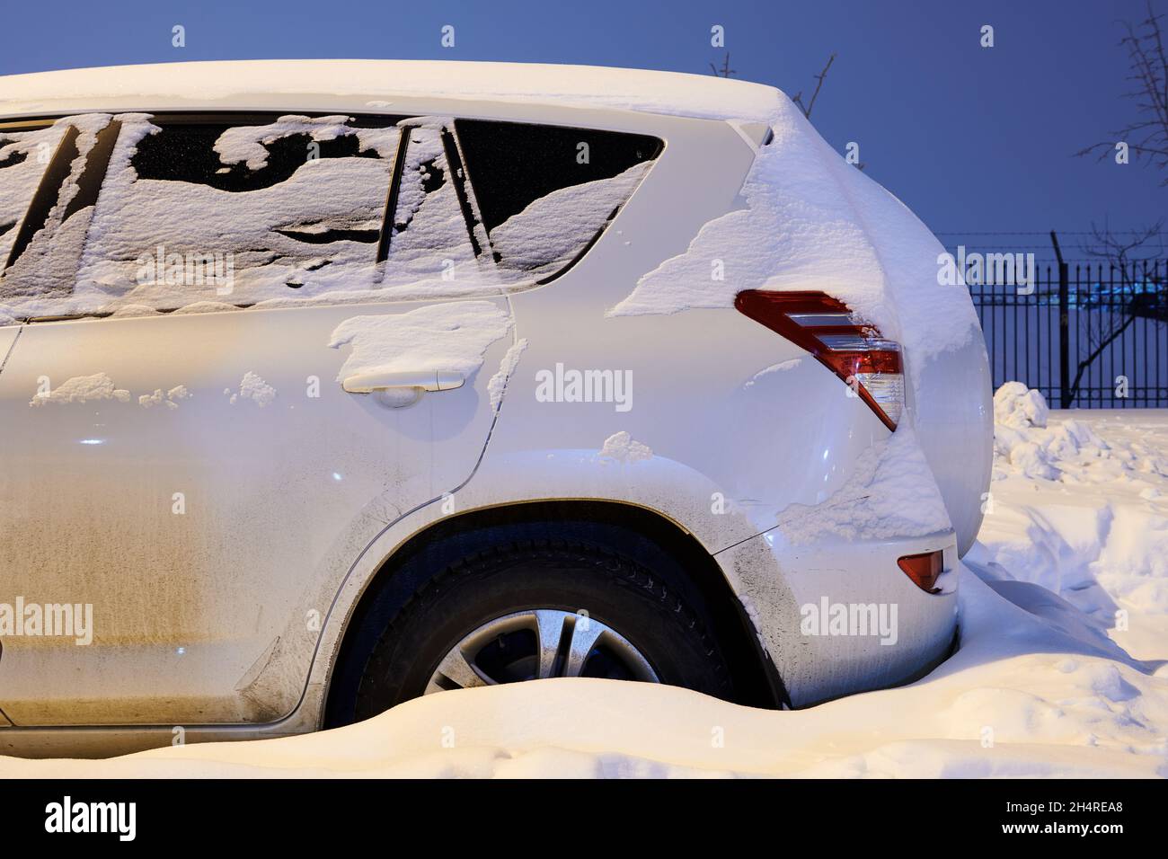 Auto bianca coperta di neve di notte. SUV parcheggiato nel cortile. Città dopo la tempesta di neve. Vista laterale. Foto Stock