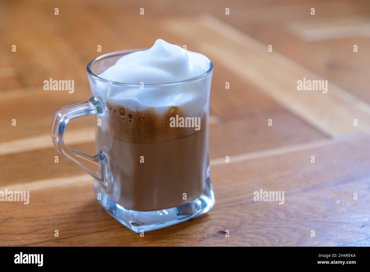 una tazza di caffè di vetro con schiuma di latte bianca sulla superficie di legno Foto Stock