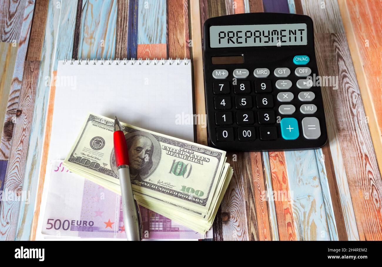 La parola PAGAMENTO ANTICIPATO su una calcolatrice, accanto a euro e dollari. Concetto di business e tasse. Foto Stock
