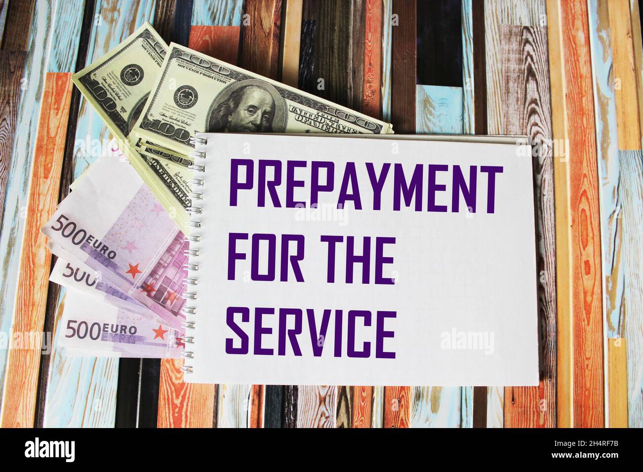 Invia il pagamento ANTICIPATO PER IL SERVIZIO su un portatile, accanto alle bollette in euro e in dollari su sfondo a righe. Foto Stock