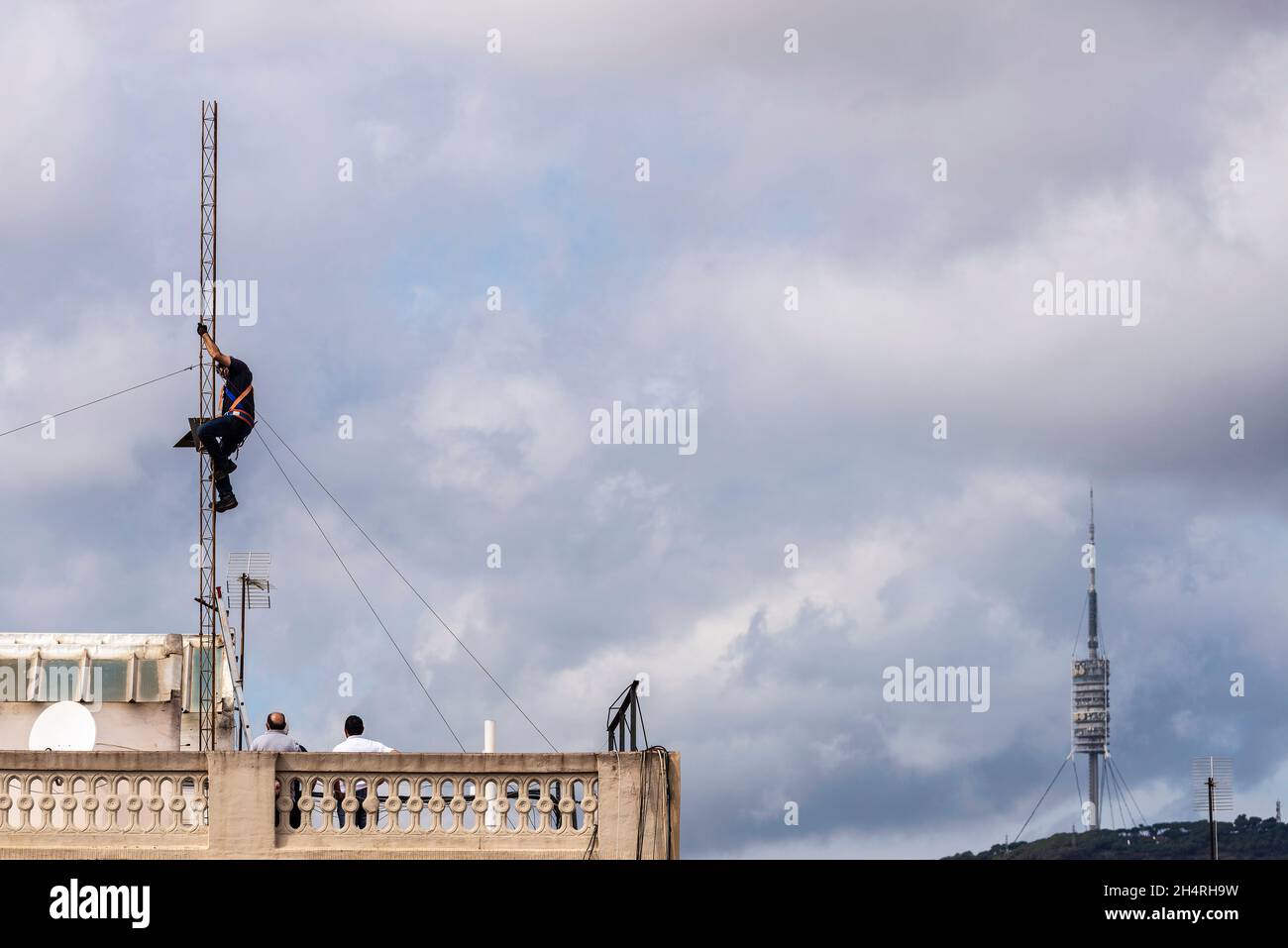 Barcellona, Spagna - 1° ottobre 2021: Torre de Collserola e un operaio edile che disassemblano un'antenna sul tetto di un edificio residenziale a Ba Foto Stock