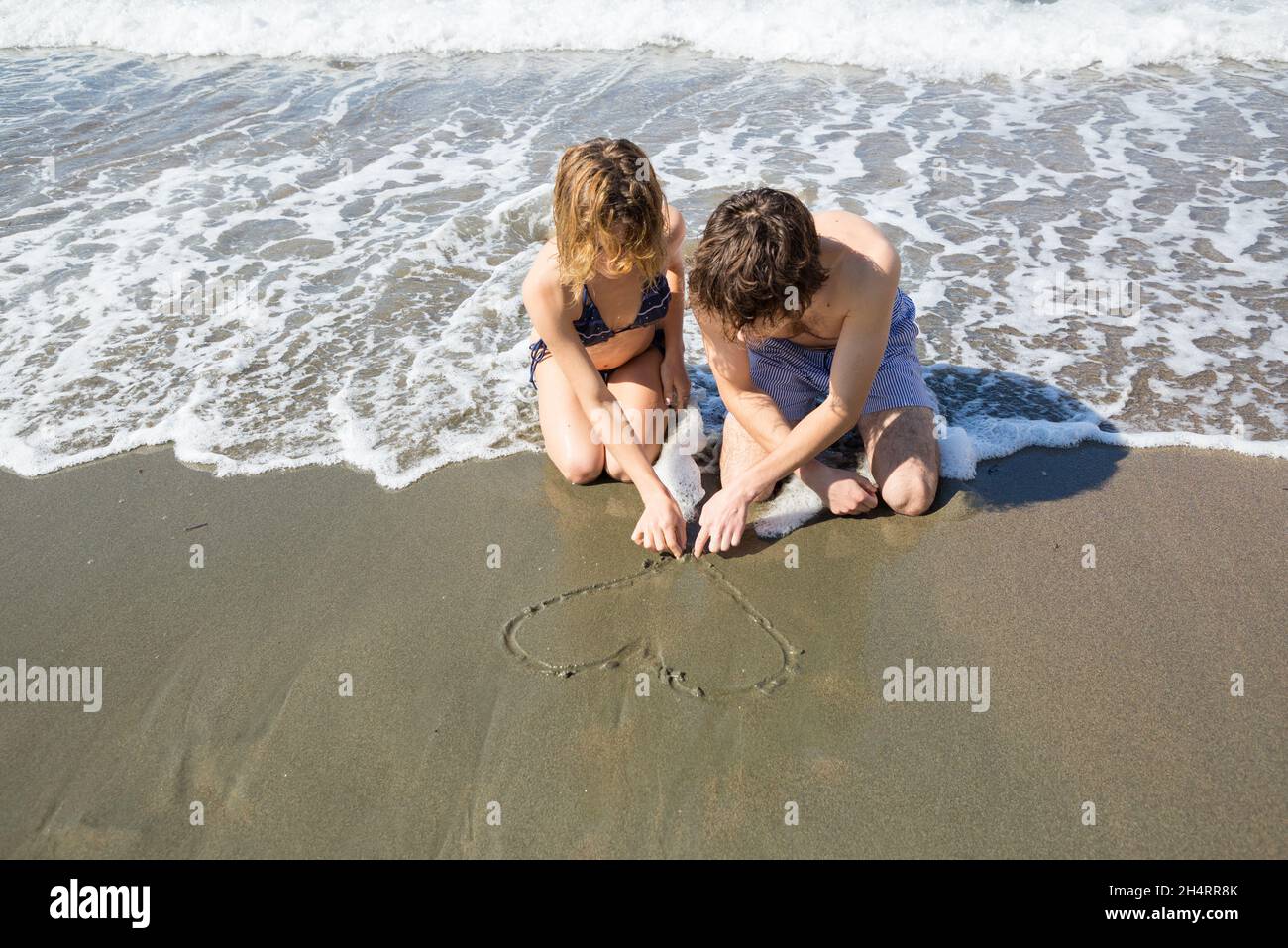 una giovane coppia innamorata, una donna e un uomo, attira un cuore sulla sabbia della costa marina. Vacanze felici, primo amore, rapporti felici, vacanze estive, Foto Stock