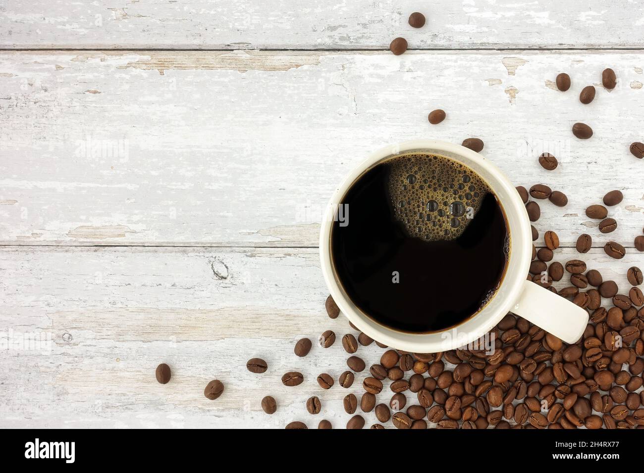 Vista dall'alto di una tazza, una tazza di caffè nero e chicchi di caffè torrefatto su legno bianco rustico resistente agli agenti atmosferici con molto spazio per la copia. Foto Stock