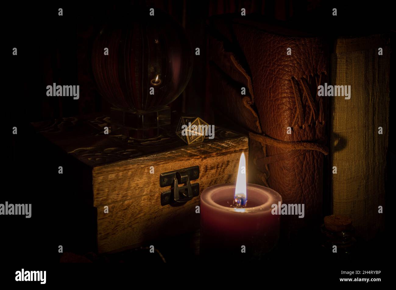 Immagine di un dado metallico a 20 lati per giocare di ruolo su una scatola di legno accanto a una sfera di cristallo e vecchi libri illuminati da lume di candela Foto Stock