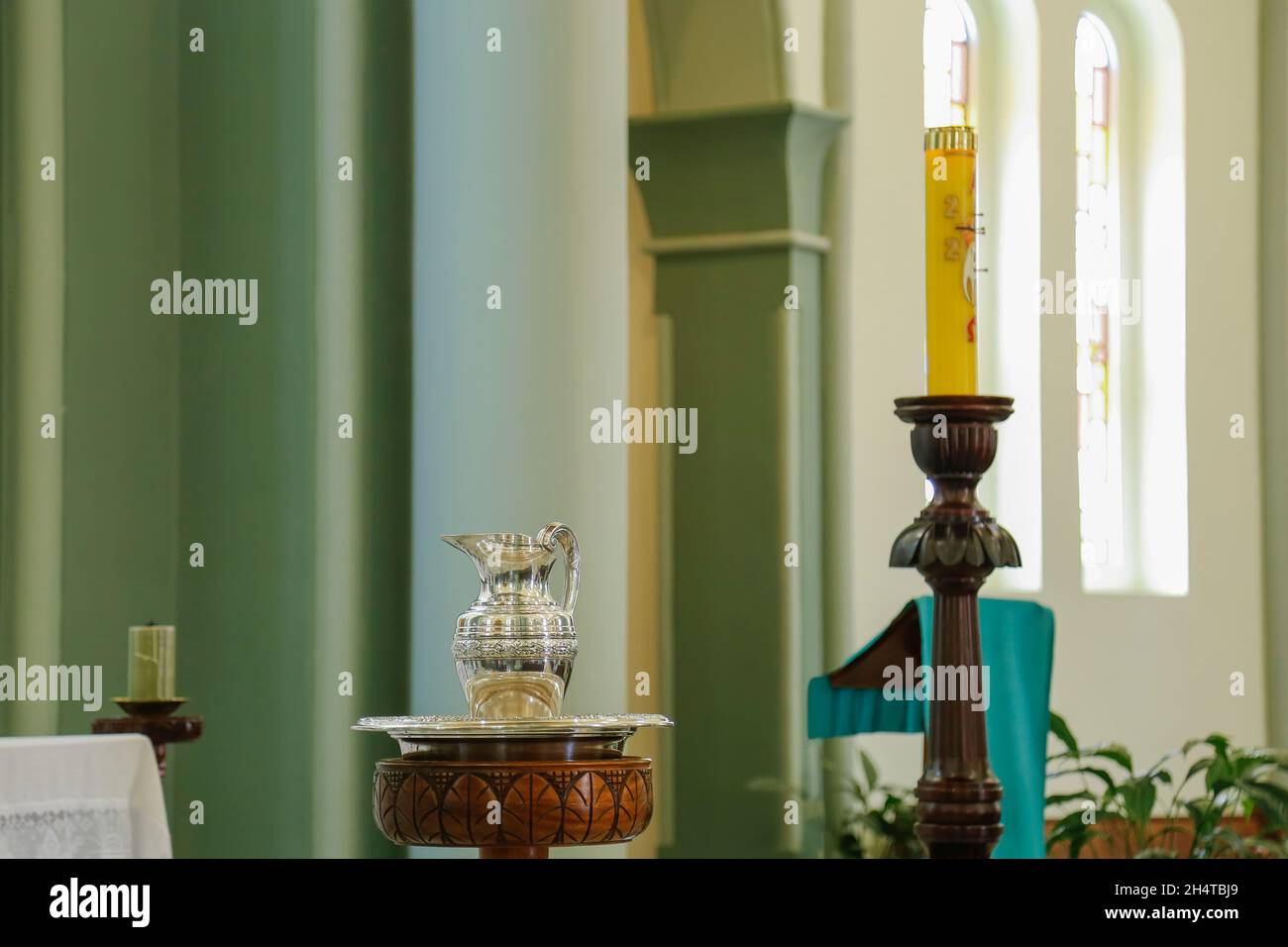 Scena illustrativa del battesimo in una chiesa cattolica con fonte battesimale, caraffa d'acqua, candele e candela pasquale Foto Stock