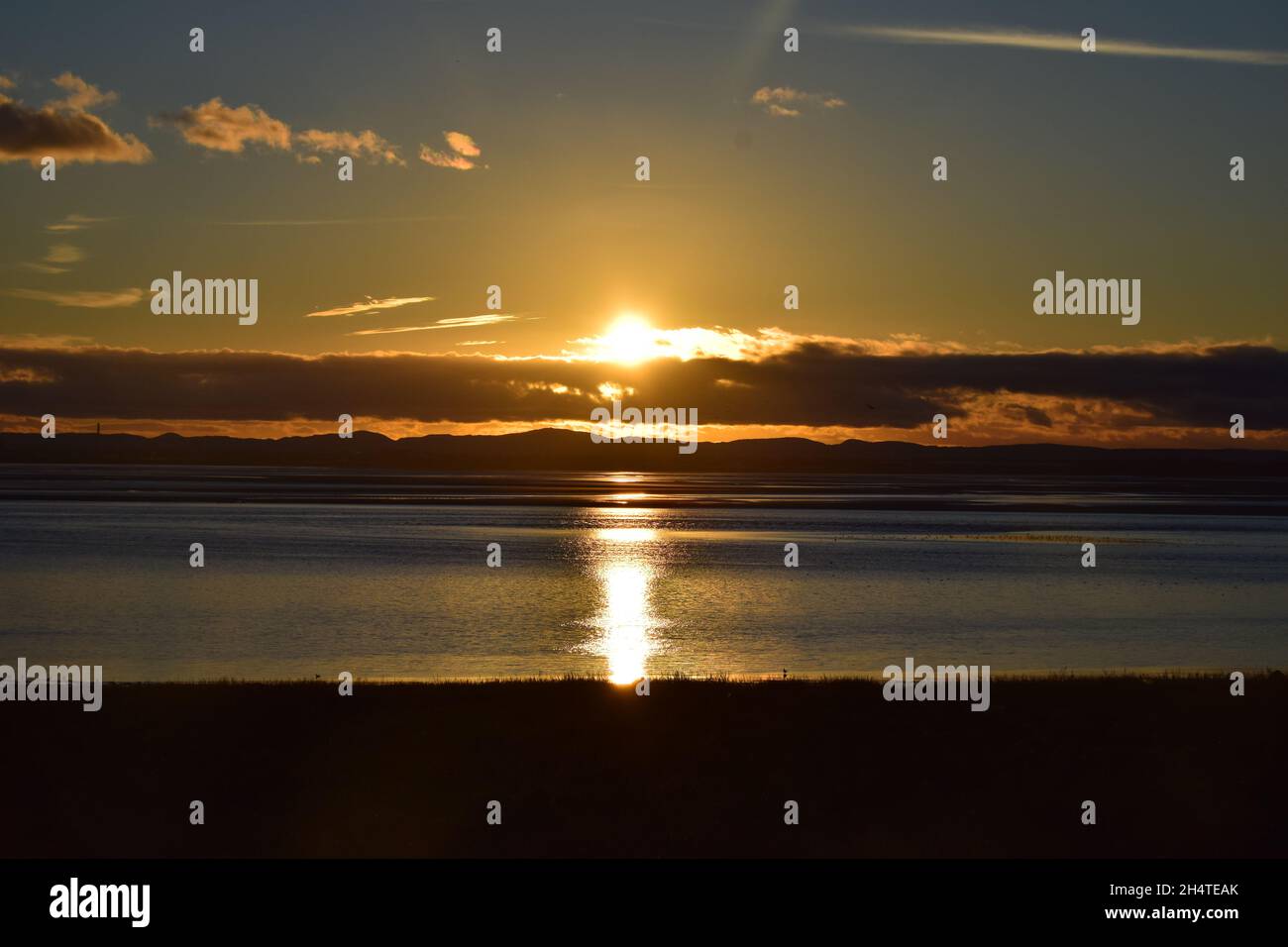 Il sole tramonta verso il basso rivelando riflessi d'acqua scintillanti e nuvole scure sopra l'estuario del fiume Mersey. Foto Stock