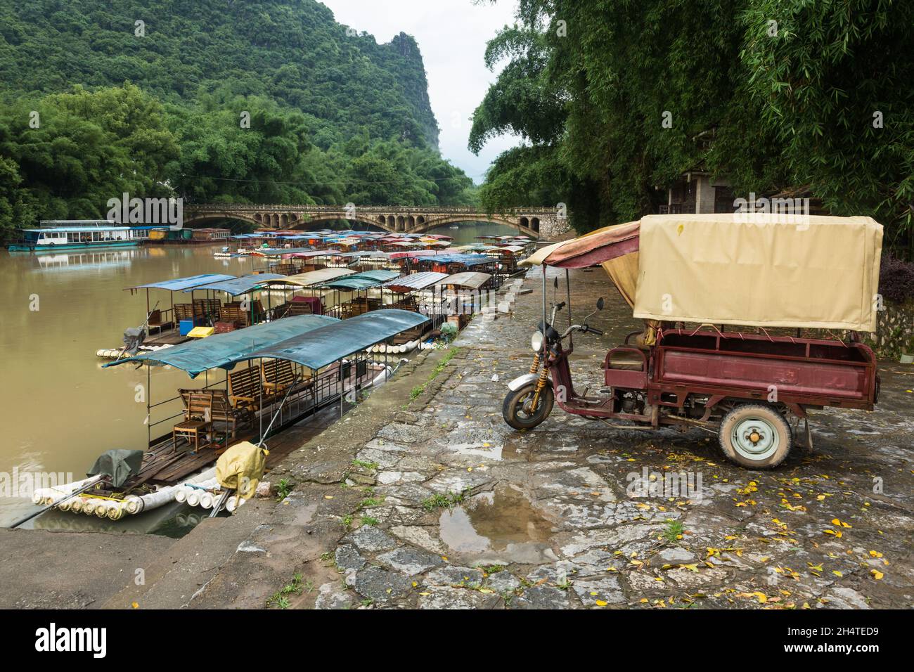 Un veicolo motorizzato a tre ruote per il trasporto di merci su un molo con imbarcazioni da tour ormeggiate. Xingping, Cina. Foto Stock