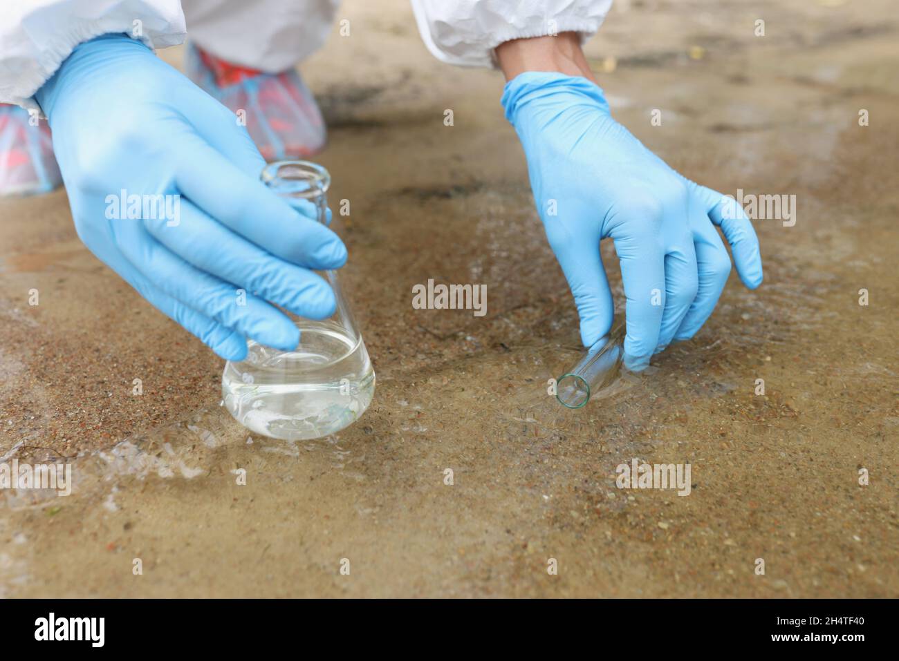 Scienziato in guanti protettivi che aspirano acqua nella provetta di prova dal primo piano del serbatoio Foto Stock
