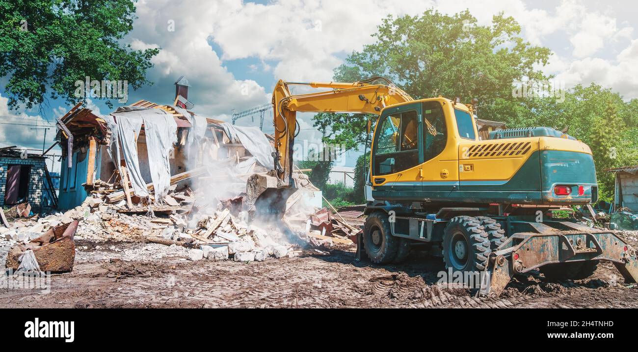 Demolizione di edifici. Processo di smantellamento della casa. L'escavatore rompe il vecchio edificio. Foto Stock