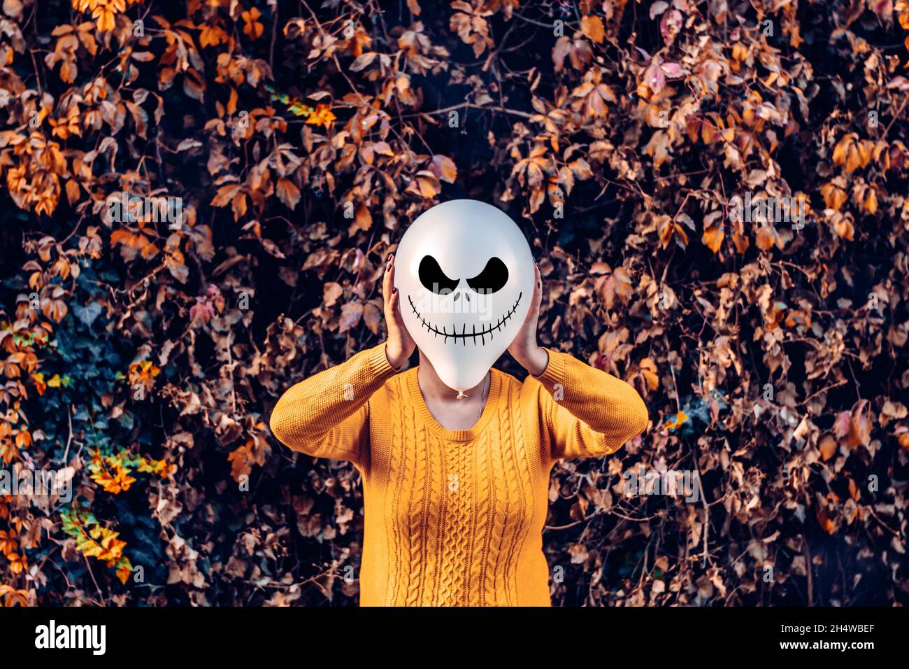 Ragazza nel cortile che tiene gonfiabile palloncino con una faccia malvagia nelle sue mani fuori happy halloween concetto Holiday card Street style Costume stagione d'autunno Foto Stock