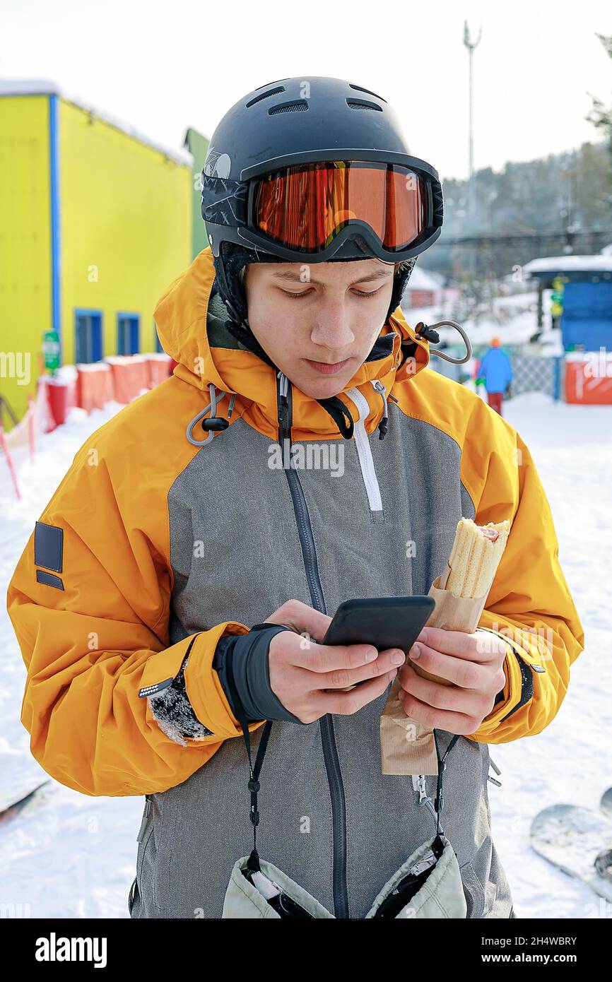 Giovane snowboarder con smartphone. Un ragazzo in una tuta sportiva  luminosa e un casco protettivo sulla pista da sci. Il giovane scrive un  messaggio di testo. Mobi Foto stock - Alamy