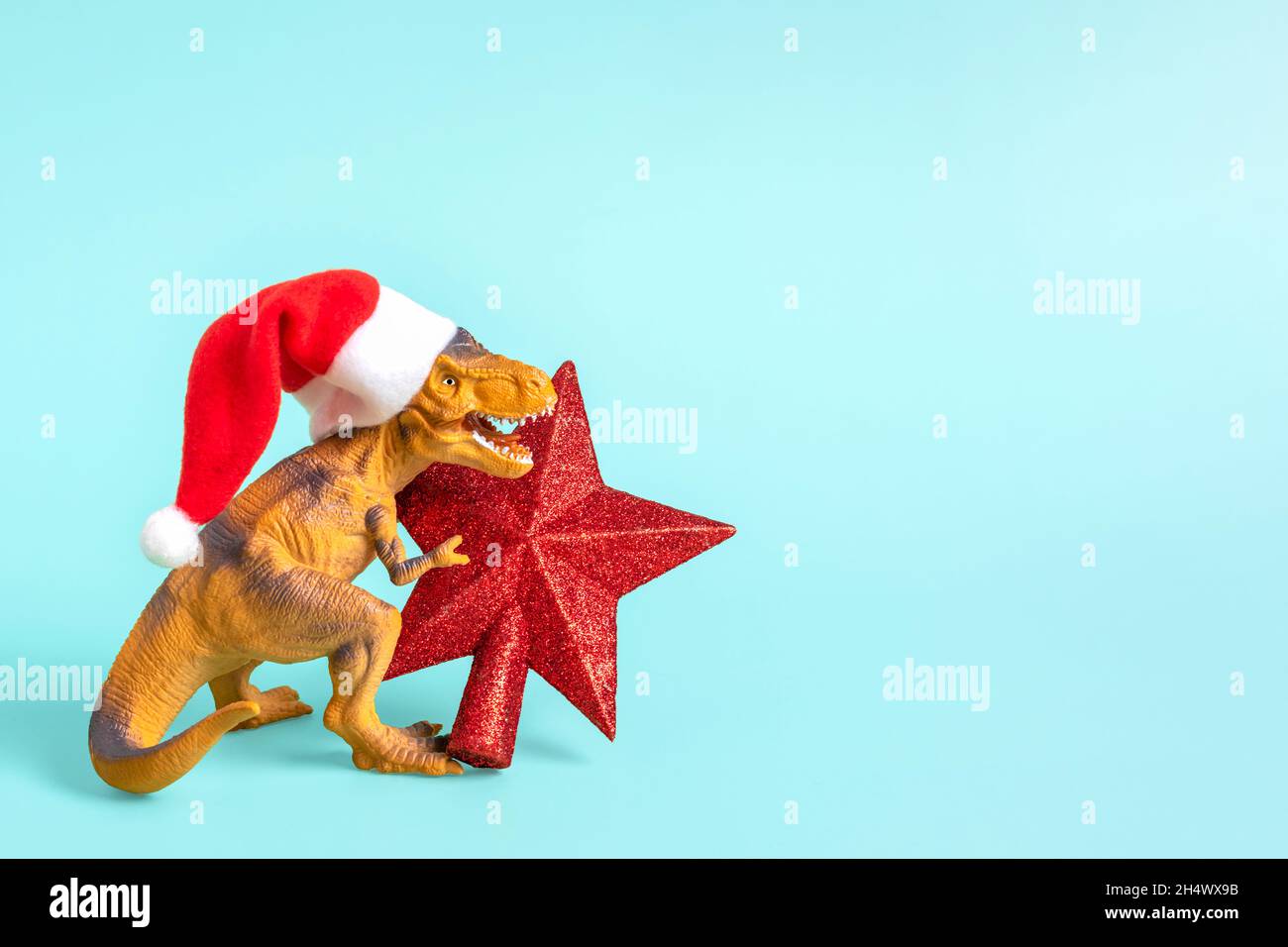 Il Rex del dinosauro in cappello rosso di Babbo Natale tiene la stella nelle relative zampe su sfondo blu la vigilia di Capodanno o la vigilia di Natale scheda di festa di arte creativa idea per Merry Foto Stock