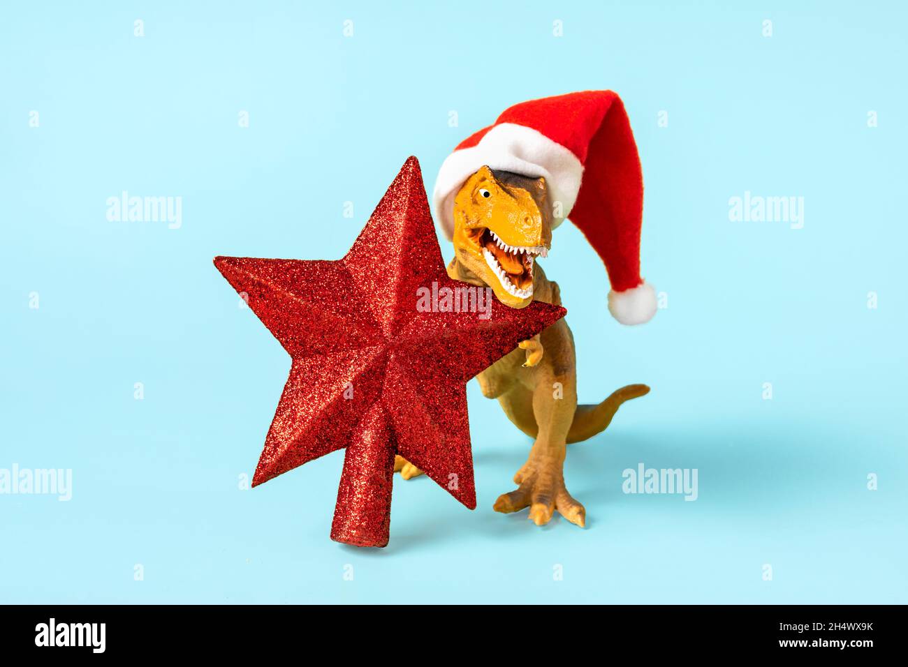 Il Rex del dinosauro in cappello rosso di Babbo Natale tiene la stella nelle relative zampe su sfondo blu la vigilia di Capodanno o la vigilia di Natale scheda di festa di arte creativa idea per Merry Foto Stock