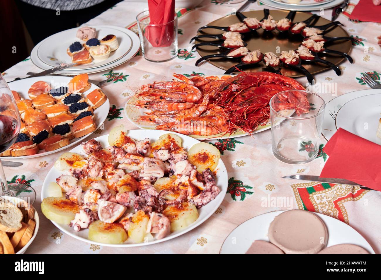 Tavolo allestito per cena di Natale con tartine di salmone e caviale, piatto di polpo galiziano, cucchiaini di confettura di peperoni con ventre di tonno, gamberi alla griglia e v Foto Stock