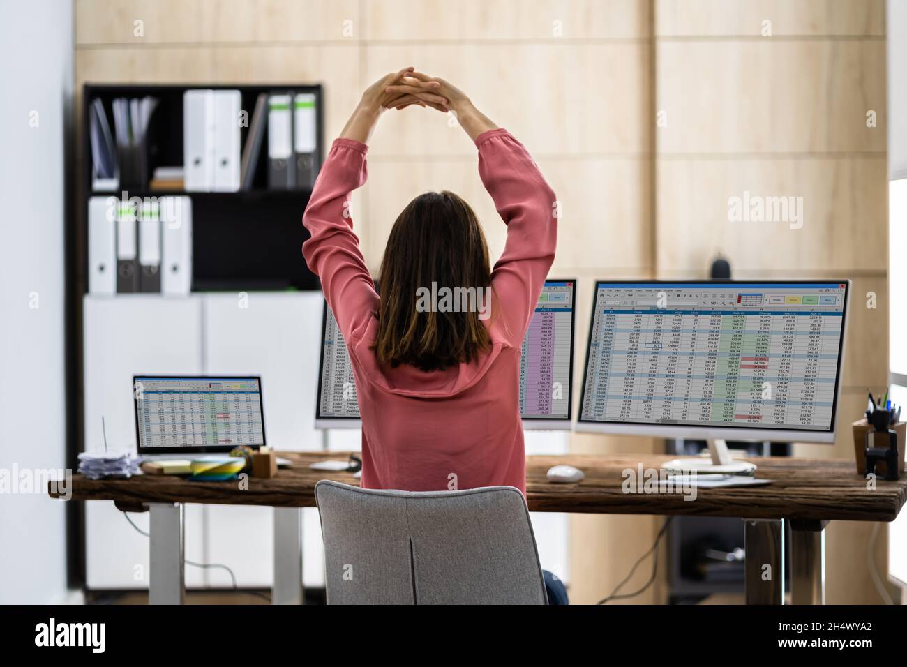 Donna di affari che fa l'esercitazione stretch alla scrivania dell'ufficio Foto Stock