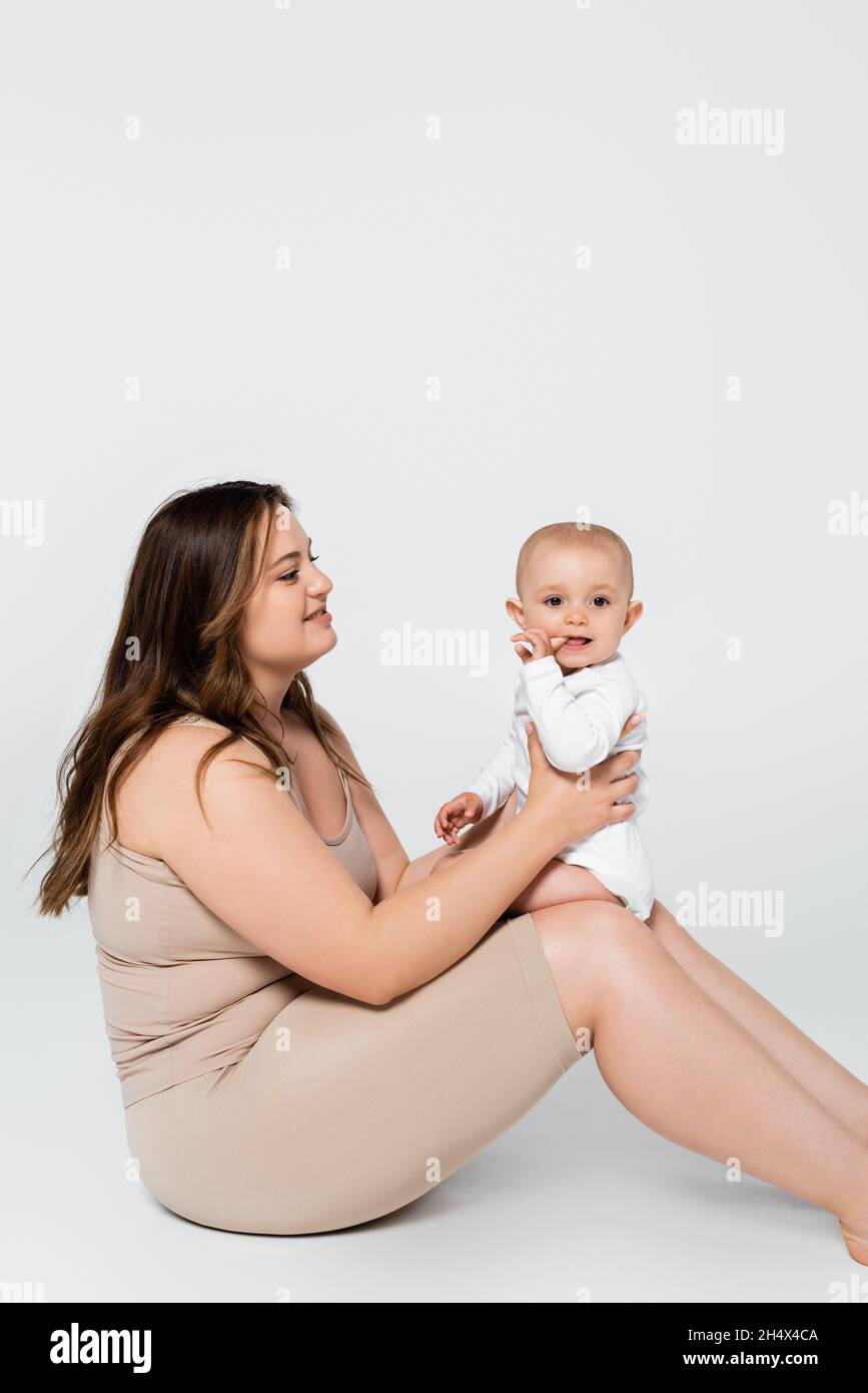 Bella più taglia donna che tiene il bambino con il dito vicino alla bocca su sfondo grigio Foto Stock