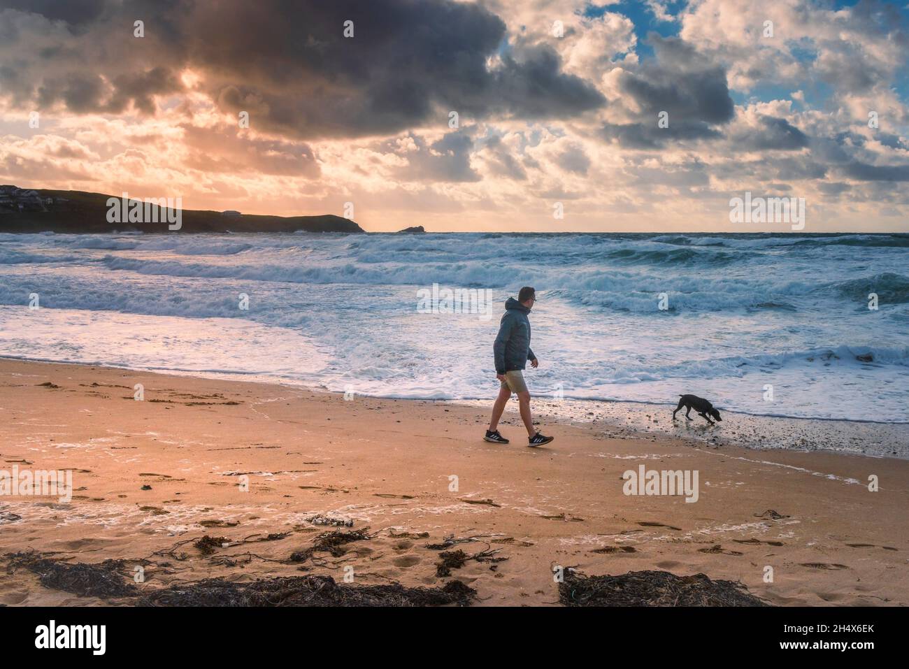 Sera luce su un uomo che cammina il suo cane lungo la costa su Fistral Beach a Newquay in Cornovaglia. Foto Stock