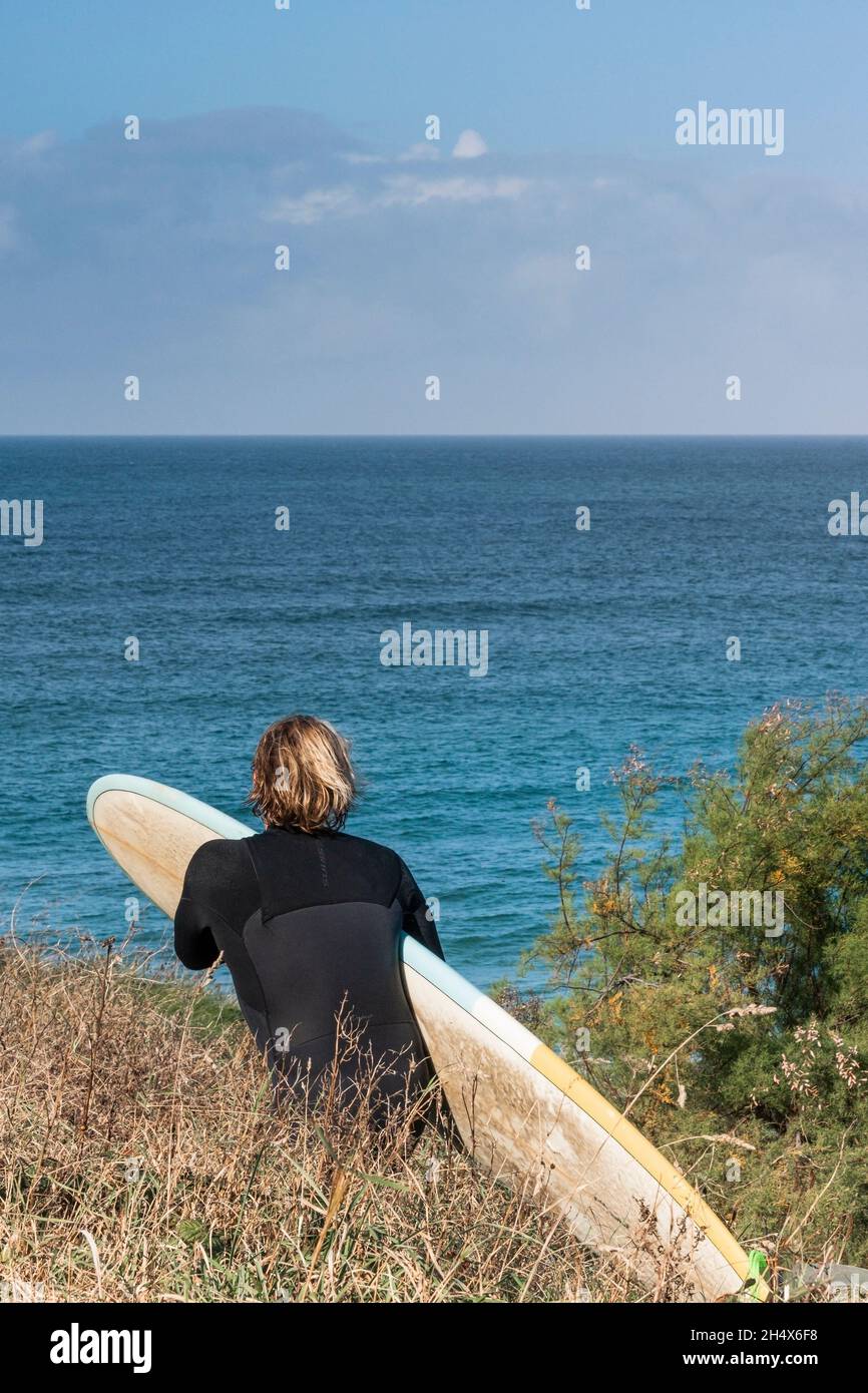 Un uomo desideroso surfista che porta la sua tavola da surf camminando lungo un sentiero costiero fino al mare in Cornovaglia. Foto Stock