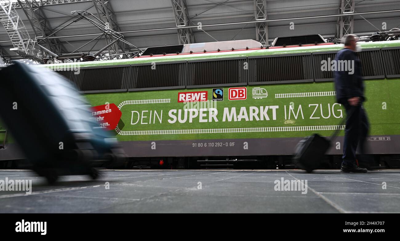 05 novembre 2021, Hessen, Francoforte sul meno: I passanti passeggiando accanto a un carro con l'iscrizione "Hessen's Supermarket Train!" Durante la presentazione del progetto temporaneo "Fair Supermarket on the Train" nella stazione centrale di Francoforte. Il treno del supermercato fiera è un supermercato completamente funzionale con cibo regionale, biologico e Fairtrade in un treno convertito. I partner sono Fairtrade, DB Regio e Rewe Region Mitte. Dopo l'inizio del 5 novembre 2021, il treno attraverserà sei città hessiani. Foto: Arne Dedert/dpa Foto Stock