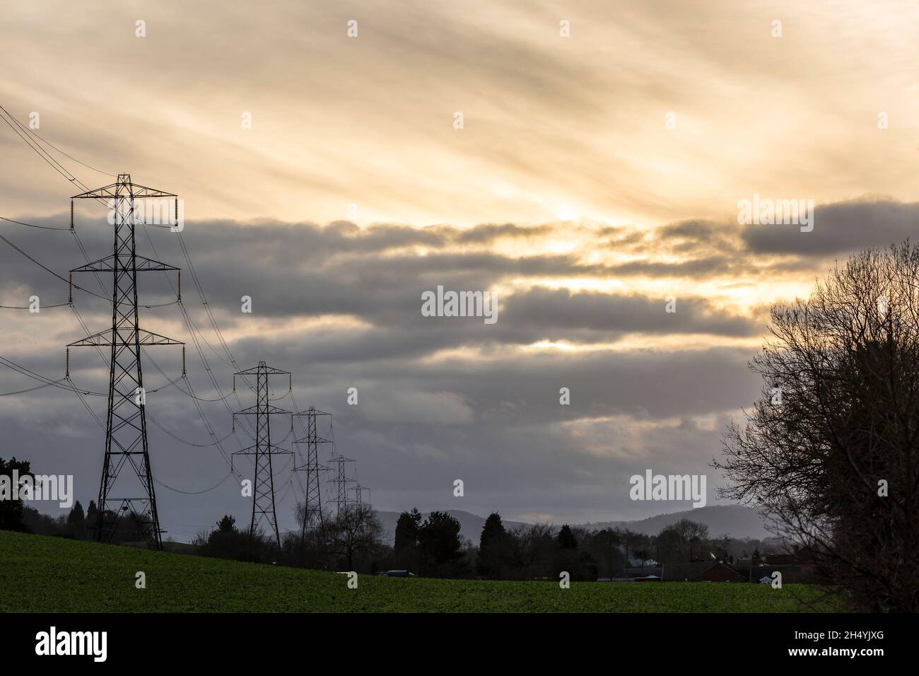 Linee elettriche aeree ad alta tensione e tralicci che trasportano energia elettrica attraverso la campagna britannica ambientando il cielo del tramonto invernale. Foto Stock