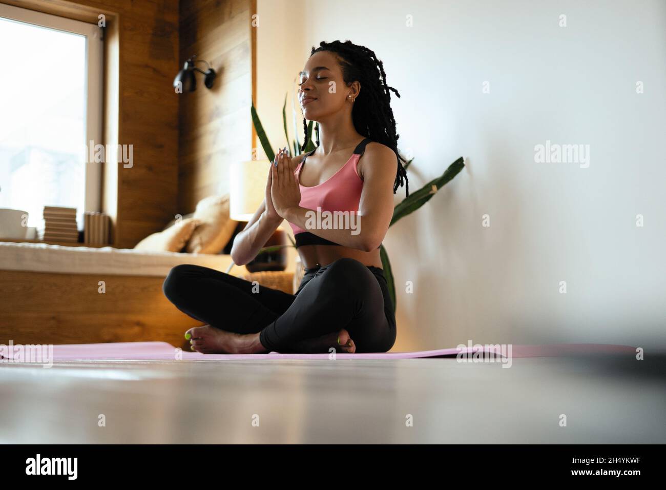 Giovane donna nera fare yoga a casa nella posizione del loto Foto Stock