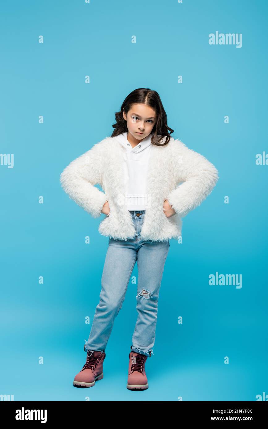 tutta la lunghezza della ragazza di età in giacca di pelliccia sintetica e stivali  invernali in piedi con le mani sui fianchi su blu Foto stock - Alamy