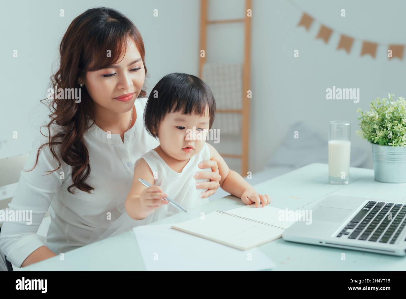 Rimani a casa mamma che lavora in remoto sul laptop mentre si prende cura del suo bambino. Foto Stock