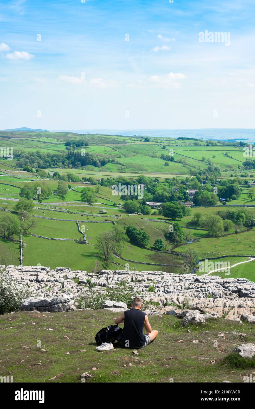 Giovane uomo viaggio da solo, vista posteriore in estate di un uomo seduto vicino al bordo della scogliera del marciapiede calcareo a Malham Cove nel Yorkshire Dales, Inghilterra Foto Stock