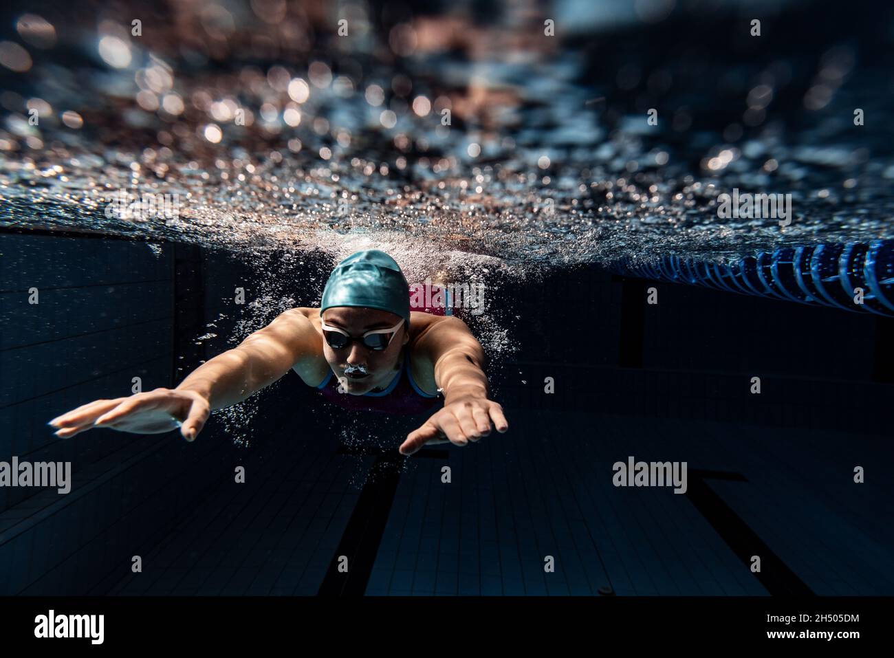 Vista subacquea dei dettagli dei movimenti di nuoto. Una nuotatrice femminile in piscina, al coperto, con berretto da nuoto e occhialini. Foto Stock