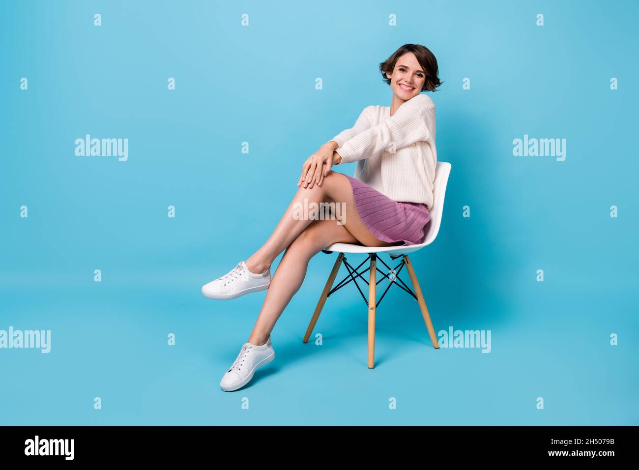 Ritratto fotografico a tutta lunghezza di una donna splendida che tocca il ginocchio seduta in sedia isolato su sfondo color pastello blu Foto Stock