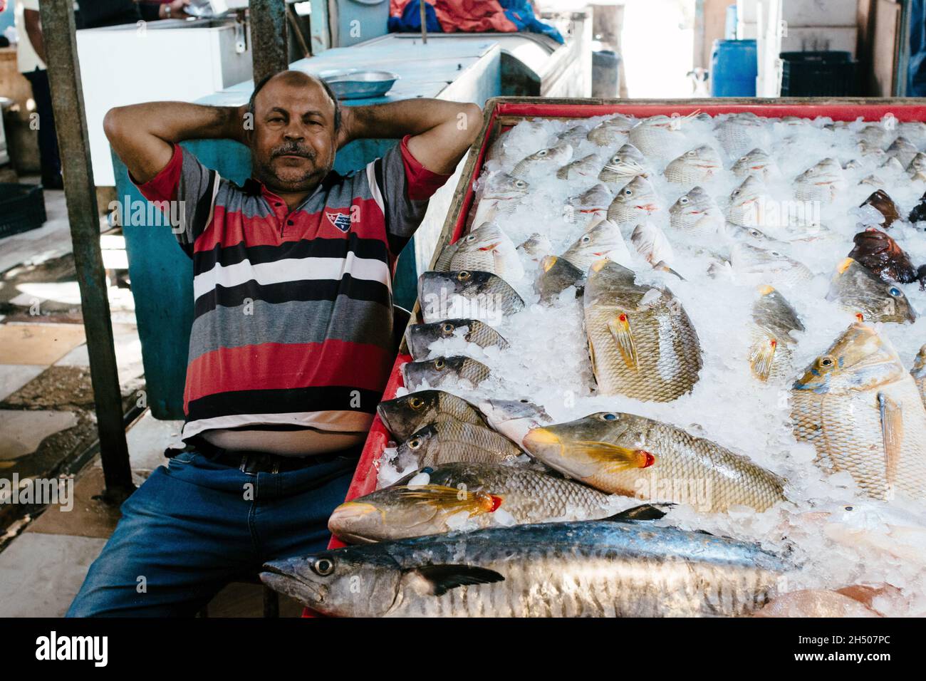 Non esclusiva: HURGHADA, EGITTO - 31 OTTOBRE 2021 - Un venditore si pende indietro con le mani dietro la testa da una stalla ad un mercato del pesce in Hurghada, Egitto. Foto Stock