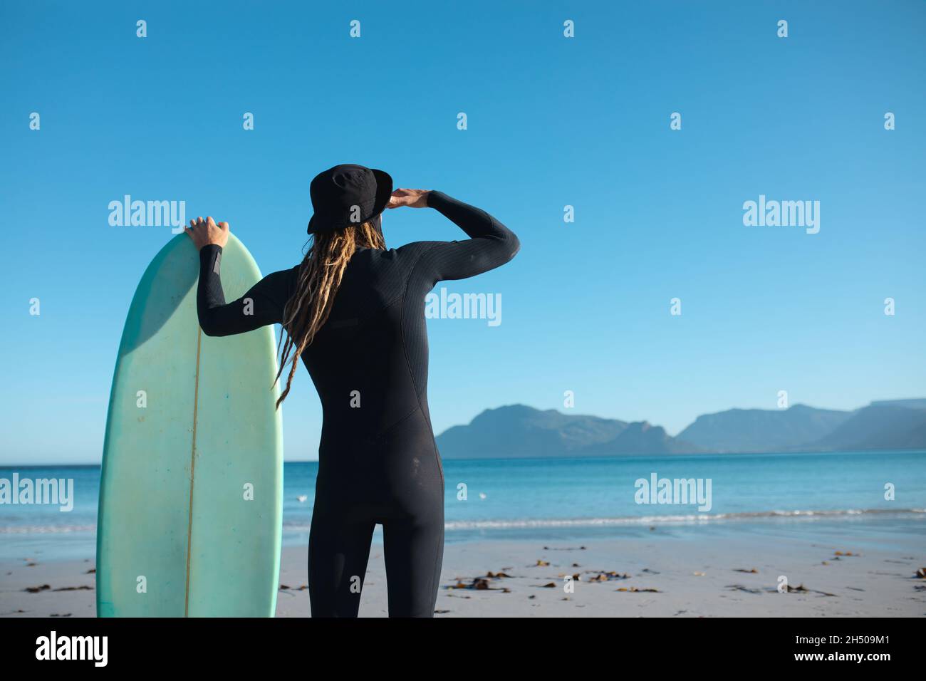 Vista posteriore dell'uomo che tiene gli occhi di protezione della tavola da surf mentre guarda lo spazio di copia sul cielo blu chiaro Foto Stock