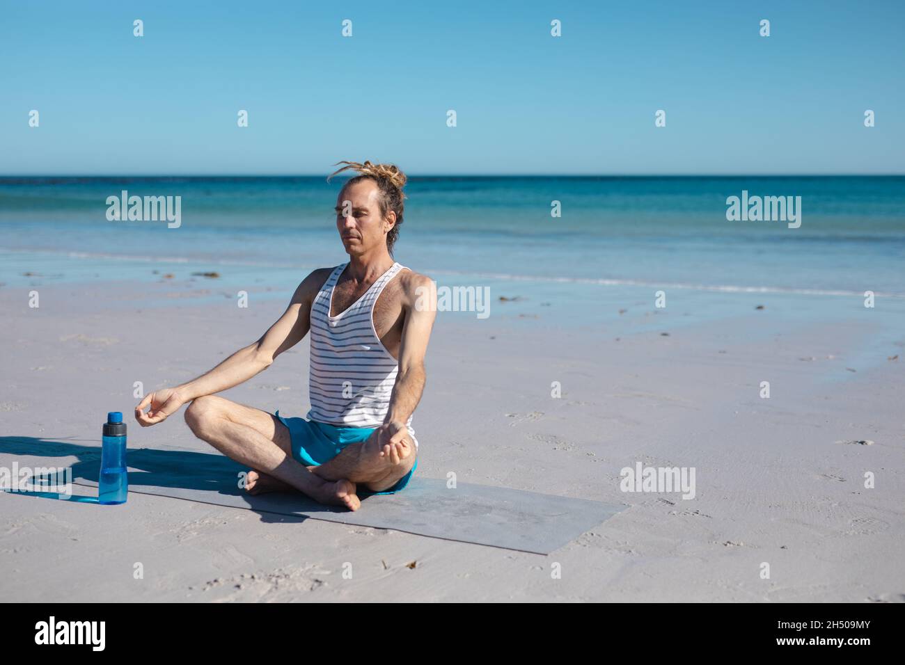 Uomo seduto a gambe incrociate che pratica la posizione di yoga loto mentre medita contro il cielo con spazio copia Foto Stock