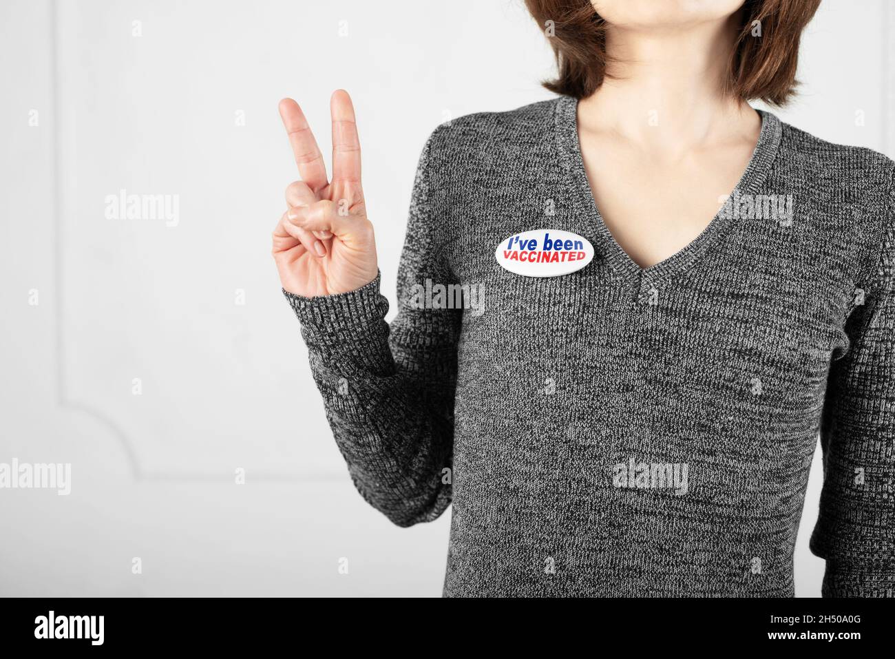 Media età femmina caucasica in maglione con bottone pin sono stato vaccinato mostrando V gesto Foto Stock